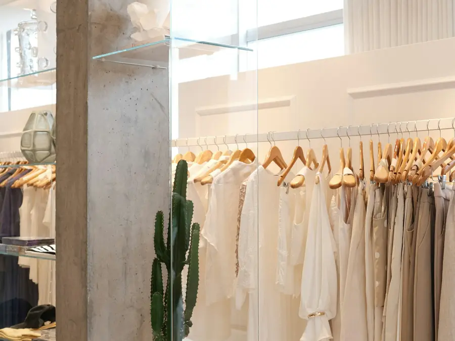 Loja clara com roupas em tons de bege e planta no canto