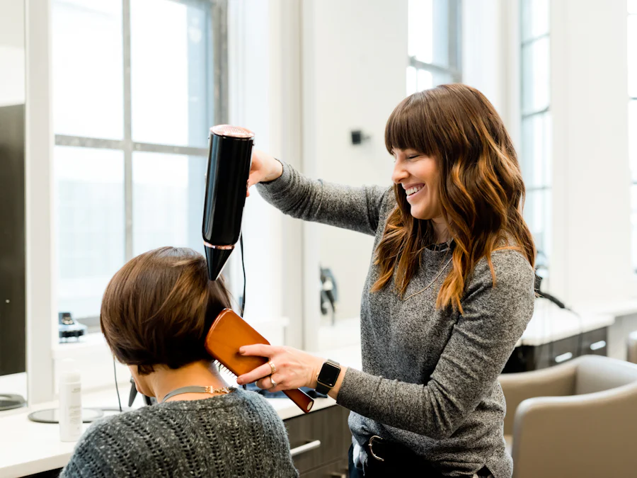 Cabeleireira sorrindo enquanto seca o cabelo de uma cliente